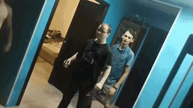a man in a black shirt is standing next to another man in a blue room .