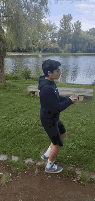 a young boy is jumping in the air in front of a lake in a park .