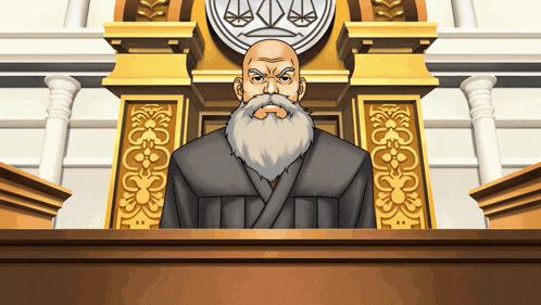 a man with a beard is sitting at a podium in front of a scales of justice emblem