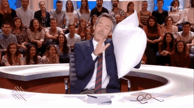 a man in a suit and tie is sitting in front of a crowd and holding a piece of paper in front of his face ..