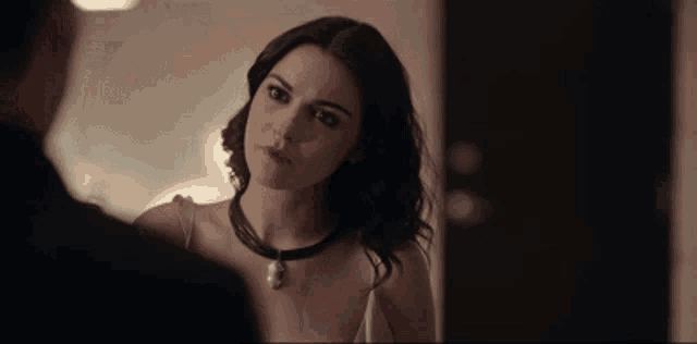 a woman is wearing a necklace and looking at a man .