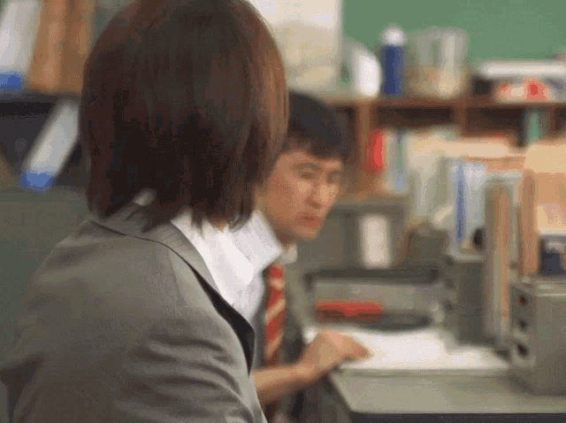 a woman in a suit and tie looks over her shoulder at a man in a tie
