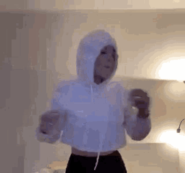 a woman wearing a white hoodie is dancing in a bedroom .