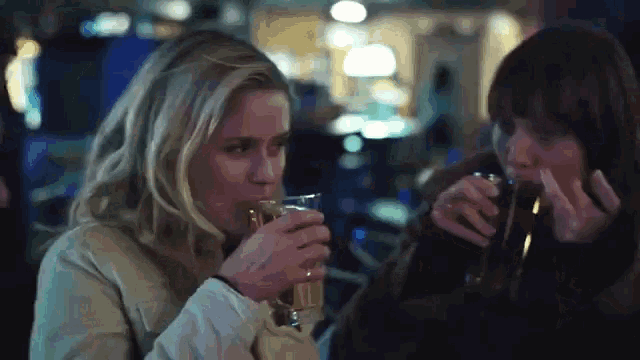 two women are drinking from glasses in a bar