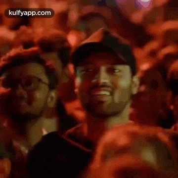 a man wearing a hat is sitting in a crowd of people and smiling .