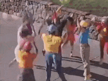 a group of children are dancing on a sidewalk in front of a stone wall .