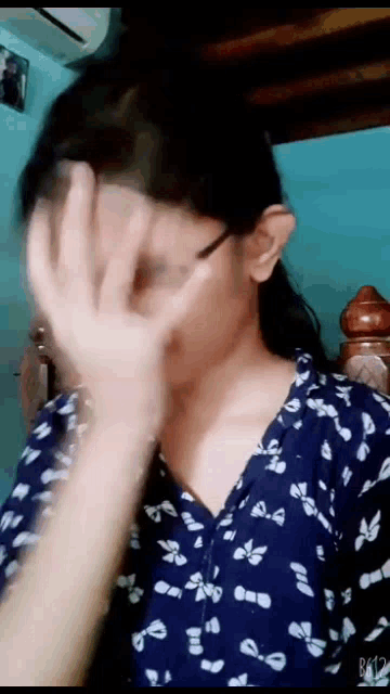 a girl is covering her face with her hand while wearing a blue shirt with white bows .