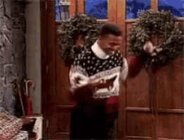 a man in a sweater is standing in front of a door with christmas wreaths on it .