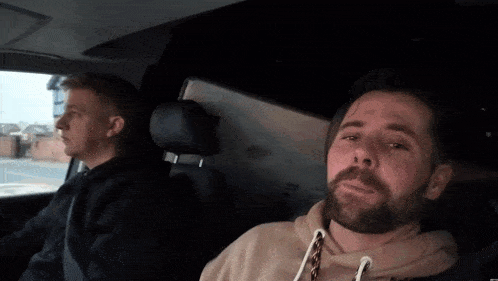 a man with a beard is sitting in the back seat of a car with another man