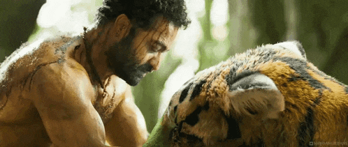 a man with a beard is petting a tiger in the woods