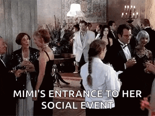 a group of people are standing in a room talking to each other and a waitress is standing in front of them .