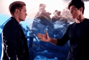 two men are standing next to each other and talking to each other in front of a painting .