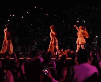 three women are dancing on a stage in front of a crowd in a dark room .