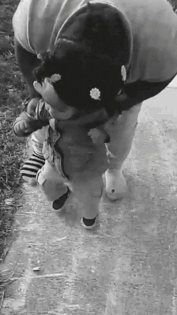 a black and white photo of a woman carrying a baby on her shoulders .