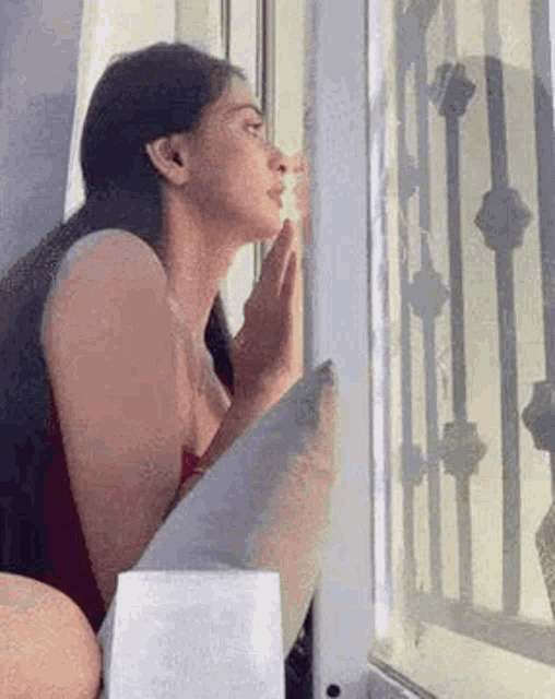 a woman is looking out of a window with her hands on her face .