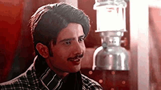 a man with a mustache and a plaid shirt is standing in front of a lantern