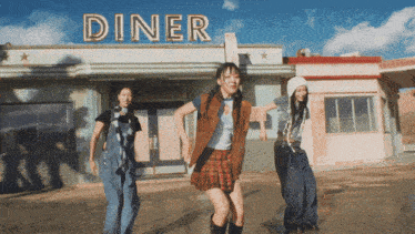 three girls are dancing in front of the diner