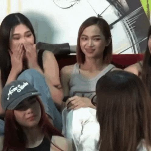 a group of young women are sitting on a couch and one of them is wearing a hat that says home studios