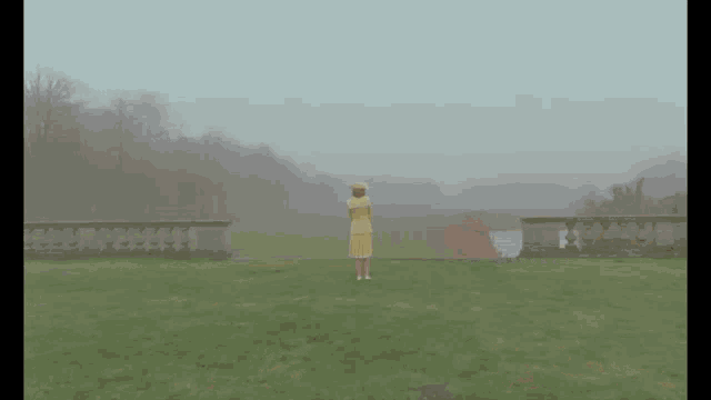 a woman in a yellow suit and hat stands in front of a brick building
