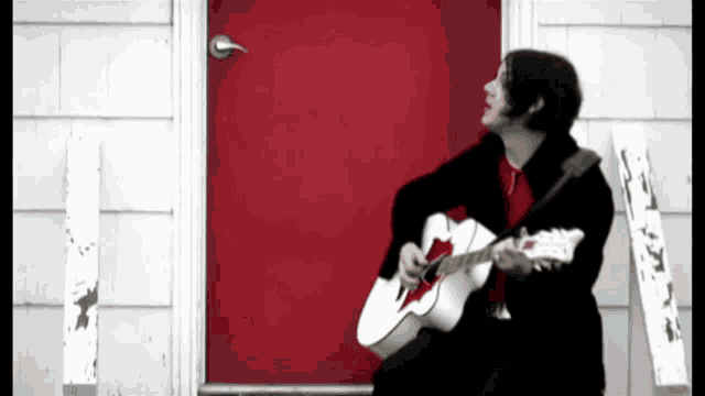 a man is playing a guitar in front of a red door