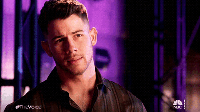 a man with a beard is standing in front of a purple background with the hashtag #thevoice