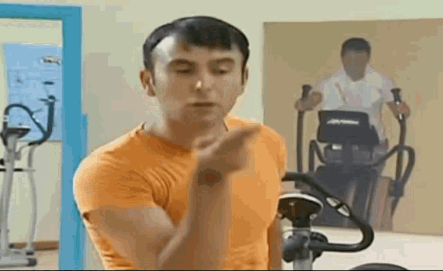 a man in an orange shirt is standing in a gym and pointing at something .