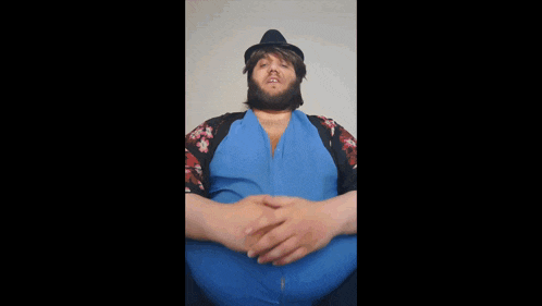 a man with a beard wearing a blue shirt and a black hat .