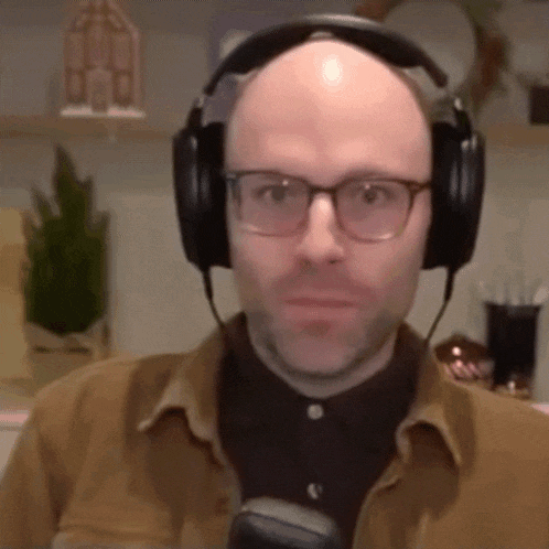 a bald man with glasses and headphones is looking at the camera .