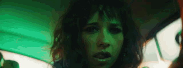 a close up of a woman 's face in a dark room with a green light behind her .