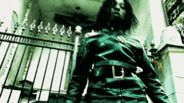 a man in a black leather jacket is standing in front of a metal fence