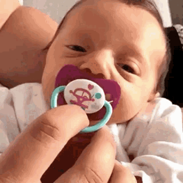 a baby is being held by a person and has a pacifier in his mouth .