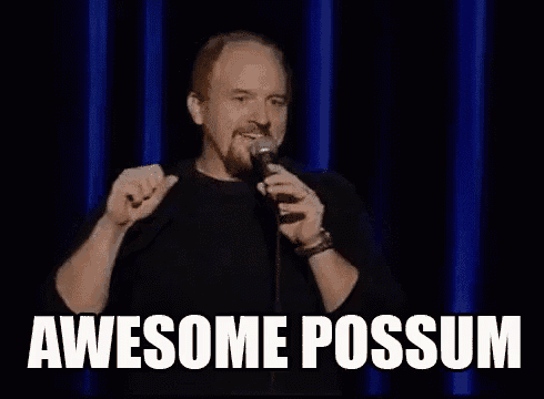 a man is holding a microphone in front of a blue curtain and saying awesome possum .