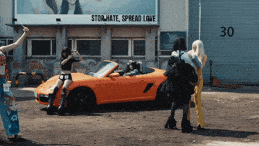 a group of women standing in front of an orange car with a sign that says " stor hate spread love "