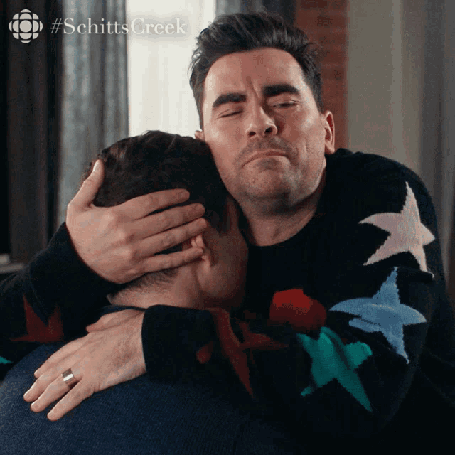two men hugging each other with #schitts creek in the background