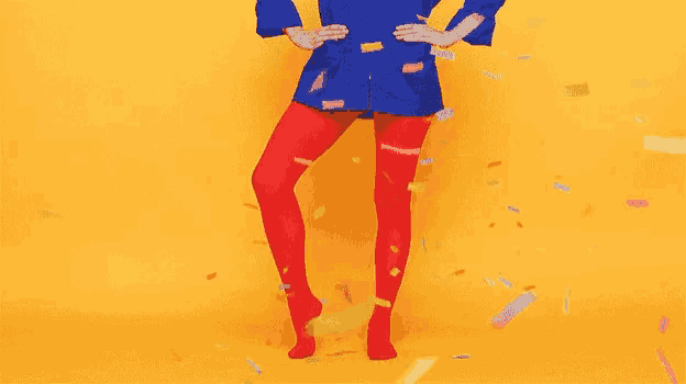 a woman in red tights and a blue jacket is standing in front of a yellow background surrounded by confetti .