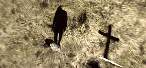 a shadow of a person is cast on a grassy field next to a cross