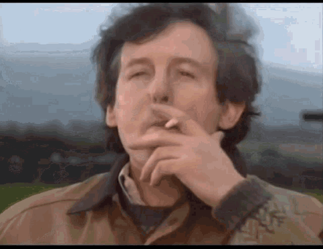 a man in a brown jacket is smoking a cigarette with his eyes closed
