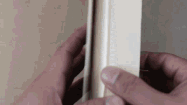 a person is holding a piece of wood in their hands and cutting it .