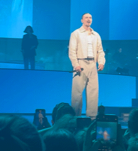 a man singing into a microphone with a crowd watching