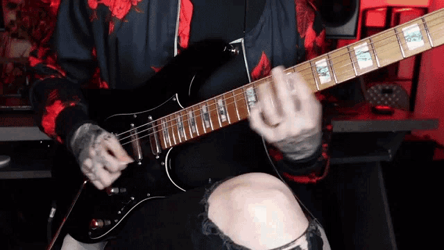 a man in a red and black sweatshirt is playing an electric guitar .