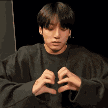 a young man is making a heart with his hands .