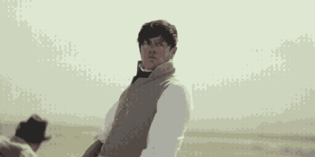 a man in a vest is standing in the desert looking at the camera