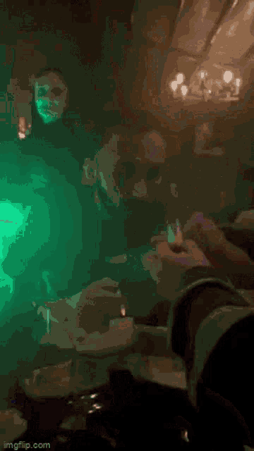 a person is sitting at a table in a dark room with a green light coming from the ceiling .