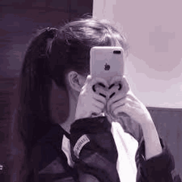 a girl is taking a selfie with her phone while making a heart with her hands .