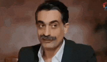 a man with a mustache is making a funny face while wearing a suit and white shirt .