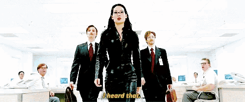 a woman in a black suit stands in front of a group of men in suits and ties and says " i heard that "