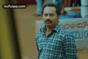 a man in a plaid shirt is standing in front of a sign that says " kulfyapp.com "