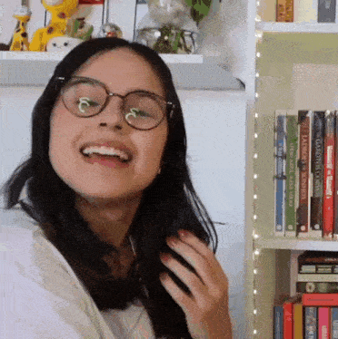 a woman wearing glasses is smiling in front of a bookshelf full of books one of which is titled lords & sons