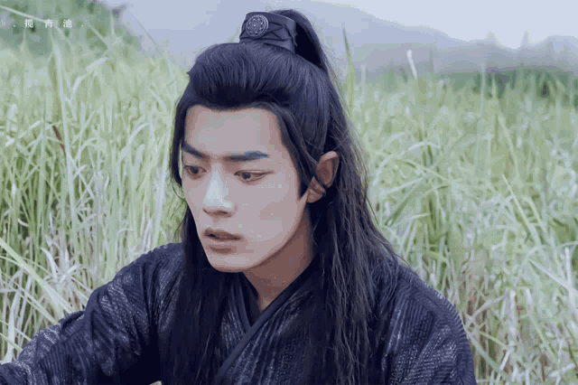 a man with long black hair and a ponytail is standing in a field
