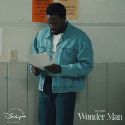 a man in a blue denim jacket is reading a piece of paper in front of a disney + sign